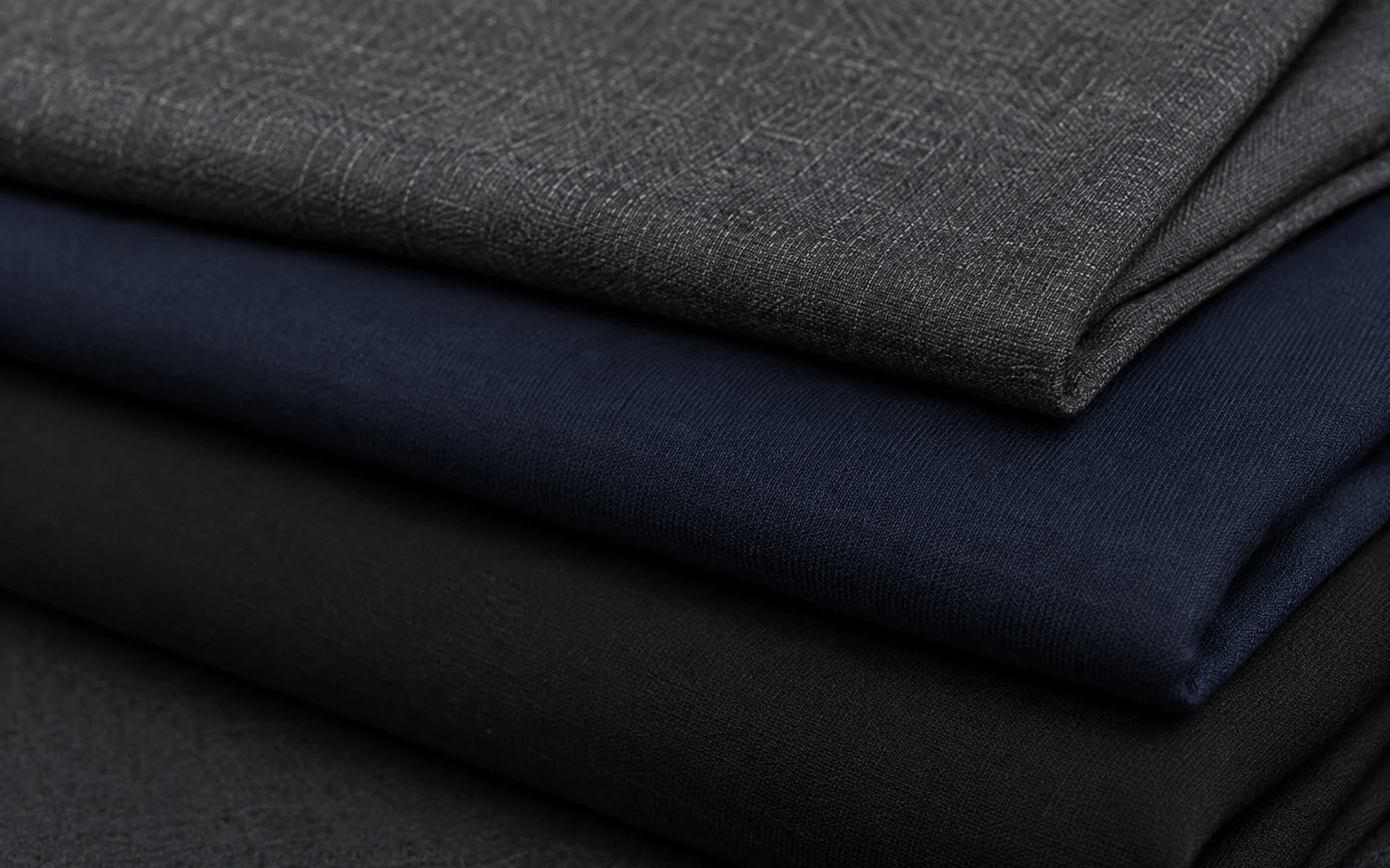 Tejidos de lana fría gris y crepé azul noche y negro doblados en capas